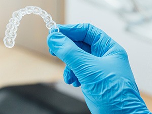 Dentist with blue glove holding clear aligner