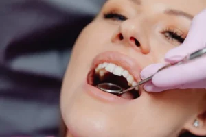 Dentist looking in woman’s mouth with small mirror